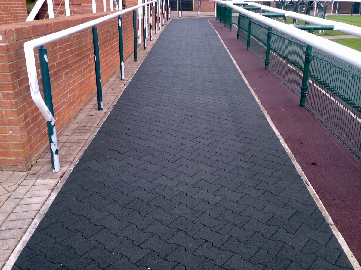 Black rubber paver walkway alongside grass landscaping