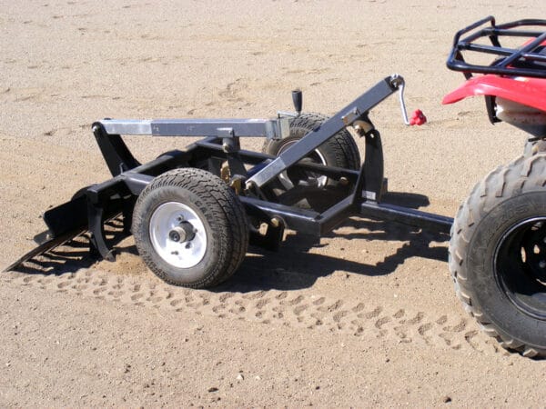 A red Arena Rake is parked in the sandy arena.