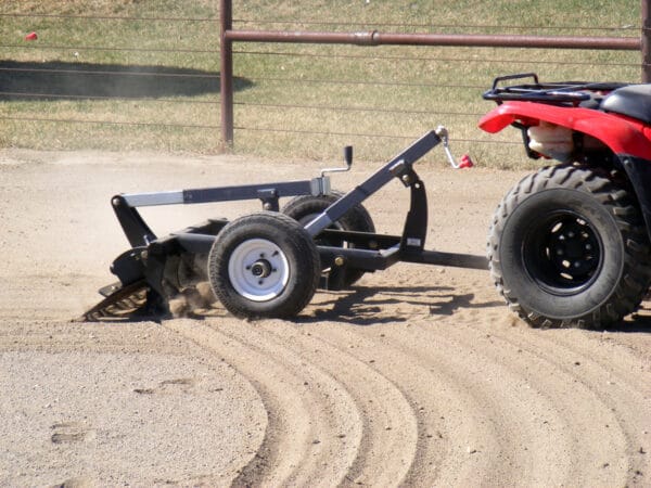 A red and black ATV pulling an Arena Rake.