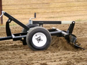 A tractor pulling an Arena Rake in the dirt.