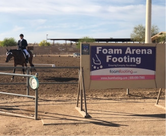 About a person riding a horse in front of a sign that says foam arena footing.