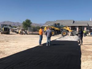 Two men standing next to a black tarp on a dirt road.