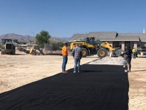 Two men standing next to a black tarp on a dirt road.