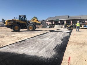 A bulldozer is working on a road in front of a house while the surrounding area functions as an arena for curious spectators.