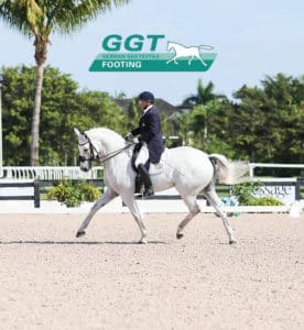 A woman riding a white horse with palm trees in the background.