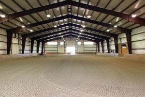 The inside of a large barn with a sand floor.