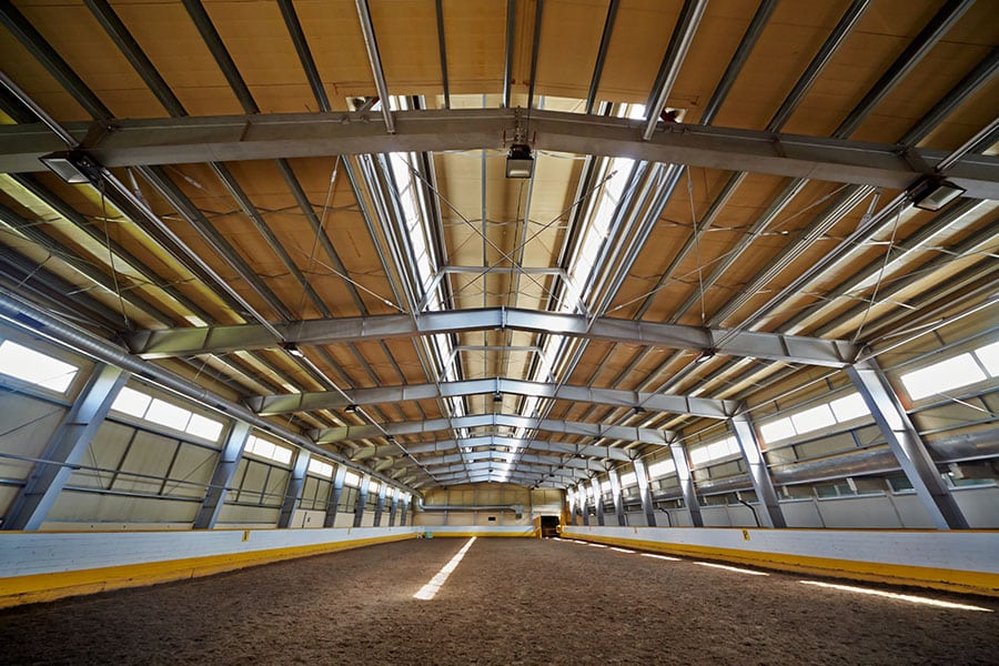 The spacious interior of a horse barn, characterized by sturdy metal beams supporting the structure.