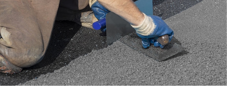 A man is laying asphalt on a road using rubber mulch.