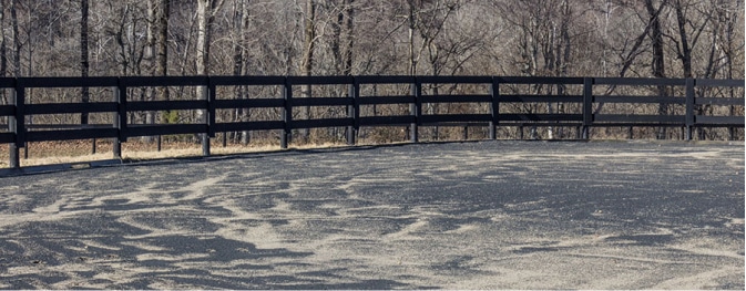 A black fenced in area with trees in the background, featuring rubber mulch.