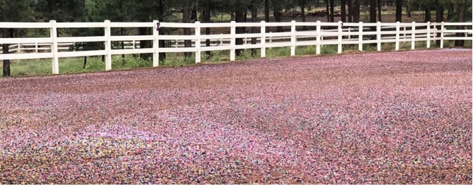 A pink gravel road with a white fence in the background, featuring a mix of rubber mulch and foam footing. A pink gravel road with a white fence in the background, featuring a mix of rubber mulch and foam footing.