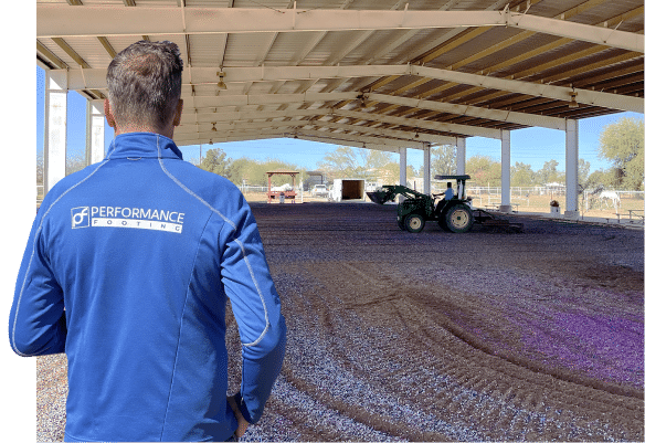A man in a blue jacket standing next to a tractor in a horse arena.