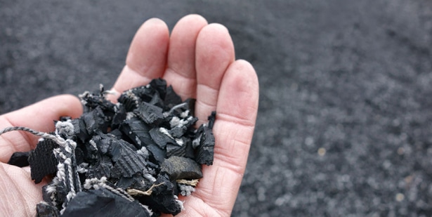 A person's hand holding a pile of black coal and comparing it to rubber mulch or foam footing.