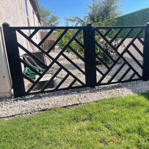 A black wrought iron gate with BaseEdge HD Steel Edging in a backyard.