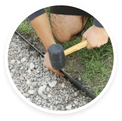 A man using a hammer to fix a pipe in the grass. A man using a hammer to fix a pipe in the grass.