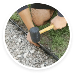 A man using a hammer to fix a pipe in the grass.