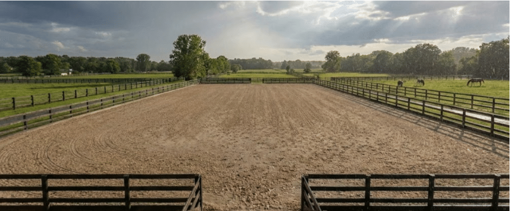 Outdoor horse arena with proper drainage system channeling water away from riding surface during heavy rainfall