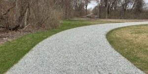 A gravel path in a park with grass and trees.